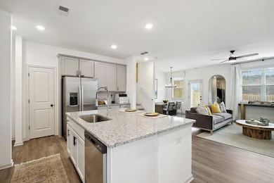 Kitchen featuring hardwood / wood-style floors, ceiling fan with notable chandelier, an island with sink, and light stone counters