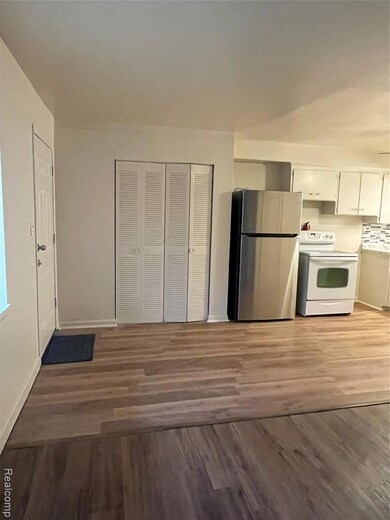 Kitchen with fridge, range, white cabinetry, dark wood-type flooring, and light countertops
