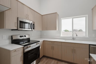 Kitchen featuring stainless steel appliances, light brown cabinets, light wood-type flooring, and modern cabinets