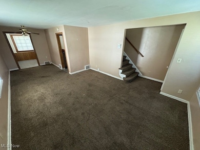 Unfurnished living room featuring carpet flooring, ceiling fan, and stairs