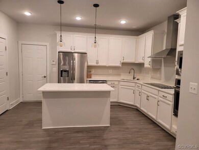 Kitchen with wall chimney range hood, hanging light fixtures, appliances with stainless steel finishes, dark wood-type flooring, and white cabinets