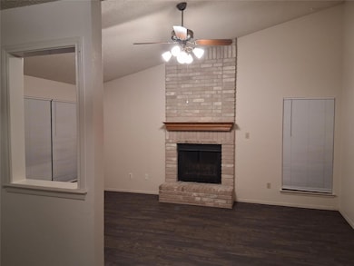 Unfurnished living room featuring vaulted ceiling, dark wood-type flooring, a brick fireplace, a textured ceiling, and a ceiling fan