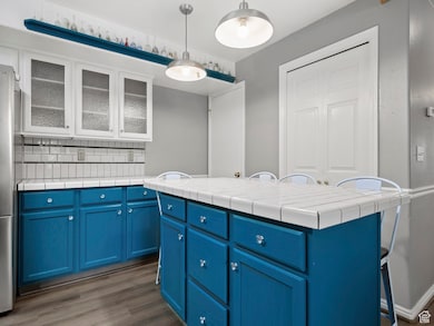 Kitchen featuring blue cabinets, a kitchen bar, glass insert cabinets, and backsplash