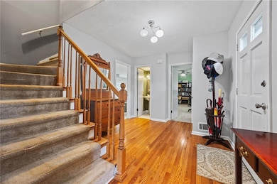 Foyer entrance with stairs, light wood-style floors, a textured ceiling, and a chandelier
