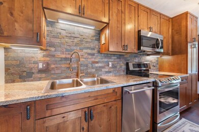 Kitchen featuring brown cabinetry, stainless steel appliances, backsplash, and light stone countertops