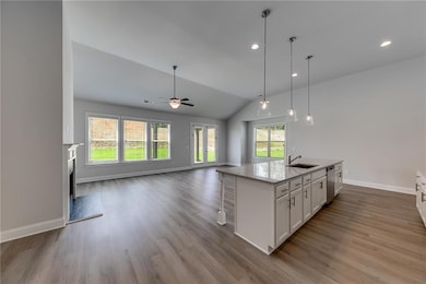 Kitchen with white cabinets, light stone counters, open floor plan, lofted ceiling, and decorative light fixtures