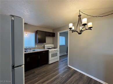 Kitchen with a baseboard heating unit, sink, white range with gas stovetop, stainless steel refrigerator, and hanging light fixtures