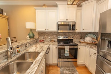 Kitchen featuring appliances with stainless steel finishes, a sink, decorative backsplash, light wood-type flooring, and ornamental molding