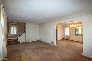 Spare room featuring a chandelier, carpet, crown molding, arched walkways, and stairway