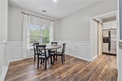 Dining space featuring a barn door, wood finished floors, wainscoting, and a decorative wall