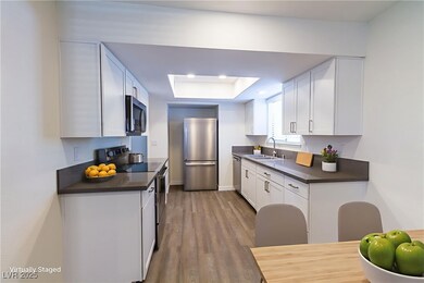 Kitchen with stainless steel appliances, a raised ceiling, white cabinets, dark wood-type flooring, and recessed lighting