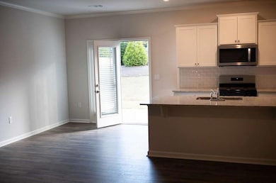 Kitchen with stainless steel microwave, range, dark wood-style floors, crown molding, and white cabinets