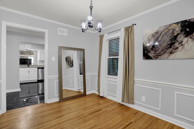 Unfurnished dining area with ornamental molding, wood finished floors, a chandelier, and a decorative wall
