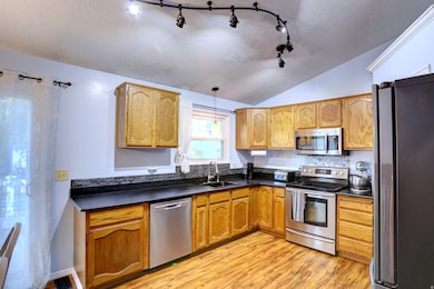Kitchen with a textured ceiling, appliances with stainless steel finishes, dark countertops, vaulted ceiling, and pendant lighting