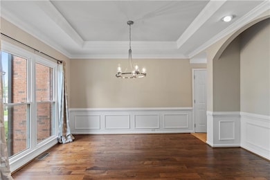 Tray ceiling, a chandelier, wood finished floors, wainscoting, and crown molding