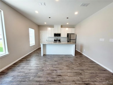 Kitchen with an island with sink, white cabinets, stainless steel appliances, decorative light fixtures, and recessed lighting