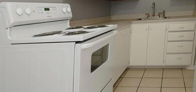 Kitchen with light tile patterned floors, sink, white cabinetry, and white range with electric stovetop