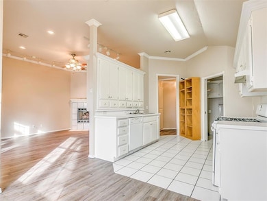 Kitchen with white appliances, ornamental molding, a ceiling fan, light wood-style floors, and white cabinetry