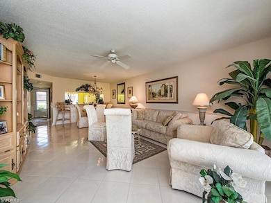 Living area with a ceiling fan, a textured ceiling, light tile patterned floors, and a chandelier