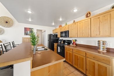 Kitchen featuring light brown cabinets, black appliances, light tile patterned floors, a kitchen island with sink, and recessed lighting
