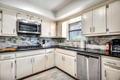 Kitchen featuring appliances with stainless steel finishes, dark countertops, decorative backsplash, and white cabinets