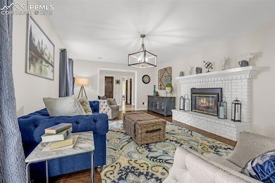 Living room with a chandelier, wood finished floors, and a brick fireplace
