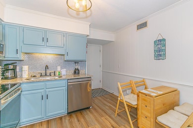 Kitchen with light wood finished floors, blue cabinetry, a sink, appliances with stainless steel finishes, and crown molding