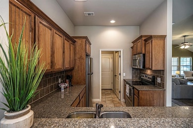 Kitchen with appliances with stainless steel finishes, a sink, dark stone countertops, a ceiling fan, and backsplash