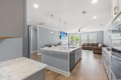 Kitchen featuring ornamental molding, a center island with sink, wood finished floors, open floor plan, and appliances with stainless steel finishes