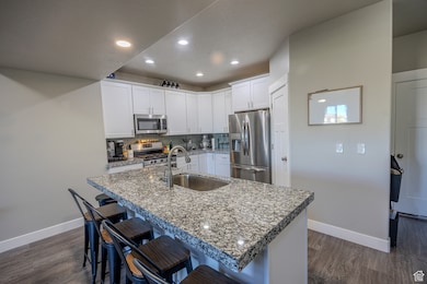 Kitchen with backsplash, white cabinets, appliances with stainless steel finishes, a kitchen bar, and dark wood-style flooring