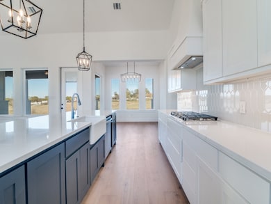 Kitchen with white cabinetry, hanging light fixtures, light wood-style flooring, a chandelier, and light stone countertops