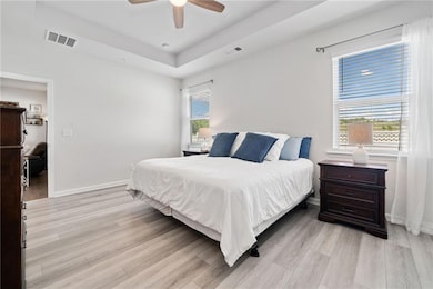 Bedroom with light wood-style floors, a raised cei