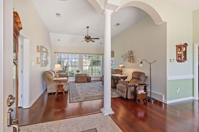 Living area with arched walkways, dark wood finished floors, vaulted ceiling, ornate columns, and ceiling fan
