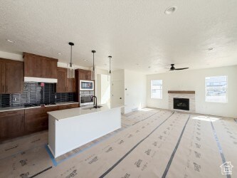 Kitchen featuring an island with sink, a fireplace, light countertops, open floor plan, and backsplash