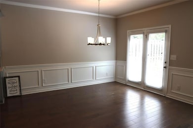 Unfurnished dining area with a chandelier, a decorative wall, wainscoting, ornamental molding, and dark wood-style flooring