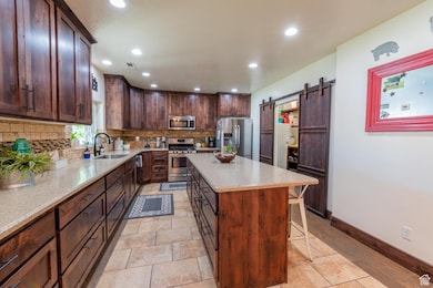 Kitchen featuring backsplash, appliances with stainless steel finishes, a barn door, a kitchen island, and light stone counters