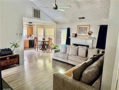 Living room with ceiling fan, light wood finished floors, high vaulted ceiling, a textured ceiling, and a fireplace