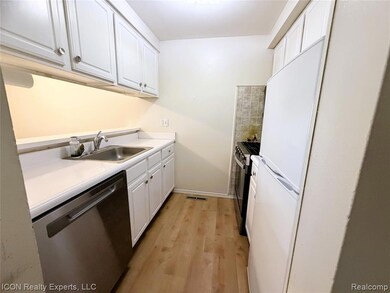 Kitchen featuring white cabinetry, stainless steel dishwasher, freestanding refrigerator, light countertops, and light wood finished floors