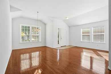 Unfurnished living room with healthy amount of natural light, a chandelier, hardwood / wood-style floors, and lofted ceiling