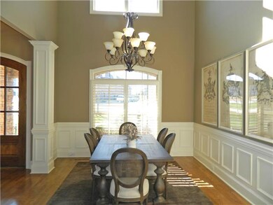Elegant Formal Dining Room with wainscoting, upper and lower  windows with lazy arch transoms, plantation shutters on the   lower windows, detailed crown molding, coffered ceiling and hardwood flooring.  