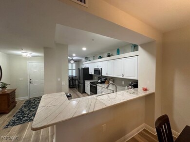 Kitchen featuring light wood-type flooring, electric range, a peninsula, stainless steel microwave, and white cabinetry