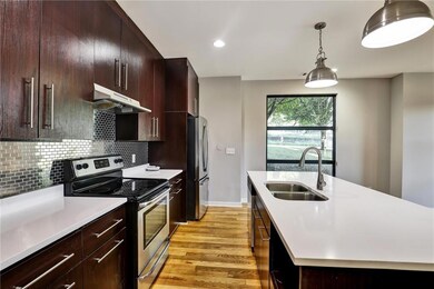 Kitchen featuring appliances with stainless steel finishes, light countertops, light wood-type flooring, under cabinet range hood, and a kitchen island with sink