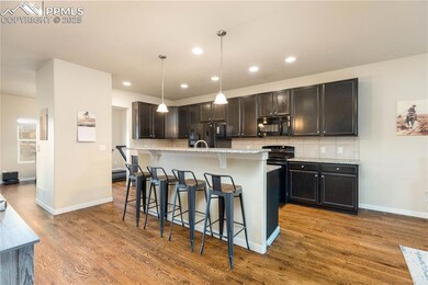 Kitchen featuring a breakfast bar, pendant lighting, light granite counters, black appliances, and a center island with sink.