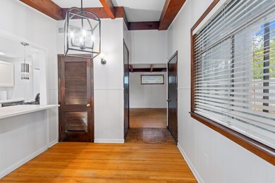 Hallway with light wood-type flooring, beam ceiling, and a chandelier