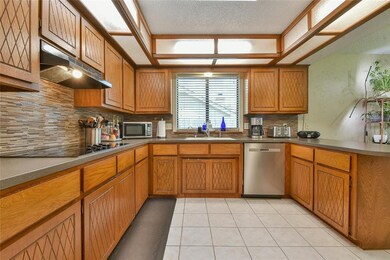 Kitchen with stainless steel appliances, under cabinet range hood, tasteful backsplash, brown cabinets, and a textured ceiling