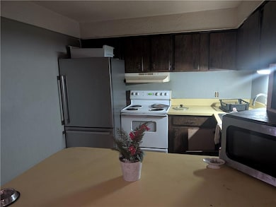 Kitchen featuring white electric range oven, freestanding refrigerator, stainless steel microwave, under cabinet range hood, and light countertops