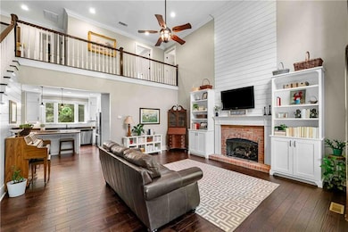 Living room featuring a ceiling fan, crown molding, a brick fireplace, a towering ceiling, and dark wood-type flooring