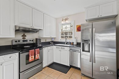 Kitchen with appliances with stainless steel finishes, white cabinets, dark countertops, light tile patterned floors, and under cabinet range hood