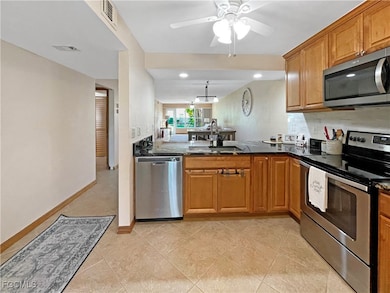 Kitchen with stainless steel appliances, dark stone counters, brown cabinetry, light tile patterned floors, and a peninsula