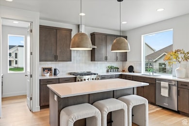 Kitchen with dark brown cabinets, a breakfast bar area, light wood-type flooring, recessed lighting, and stainless steel appliances